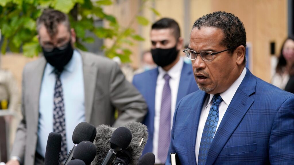 A man in blue suit and tie next to microphones.