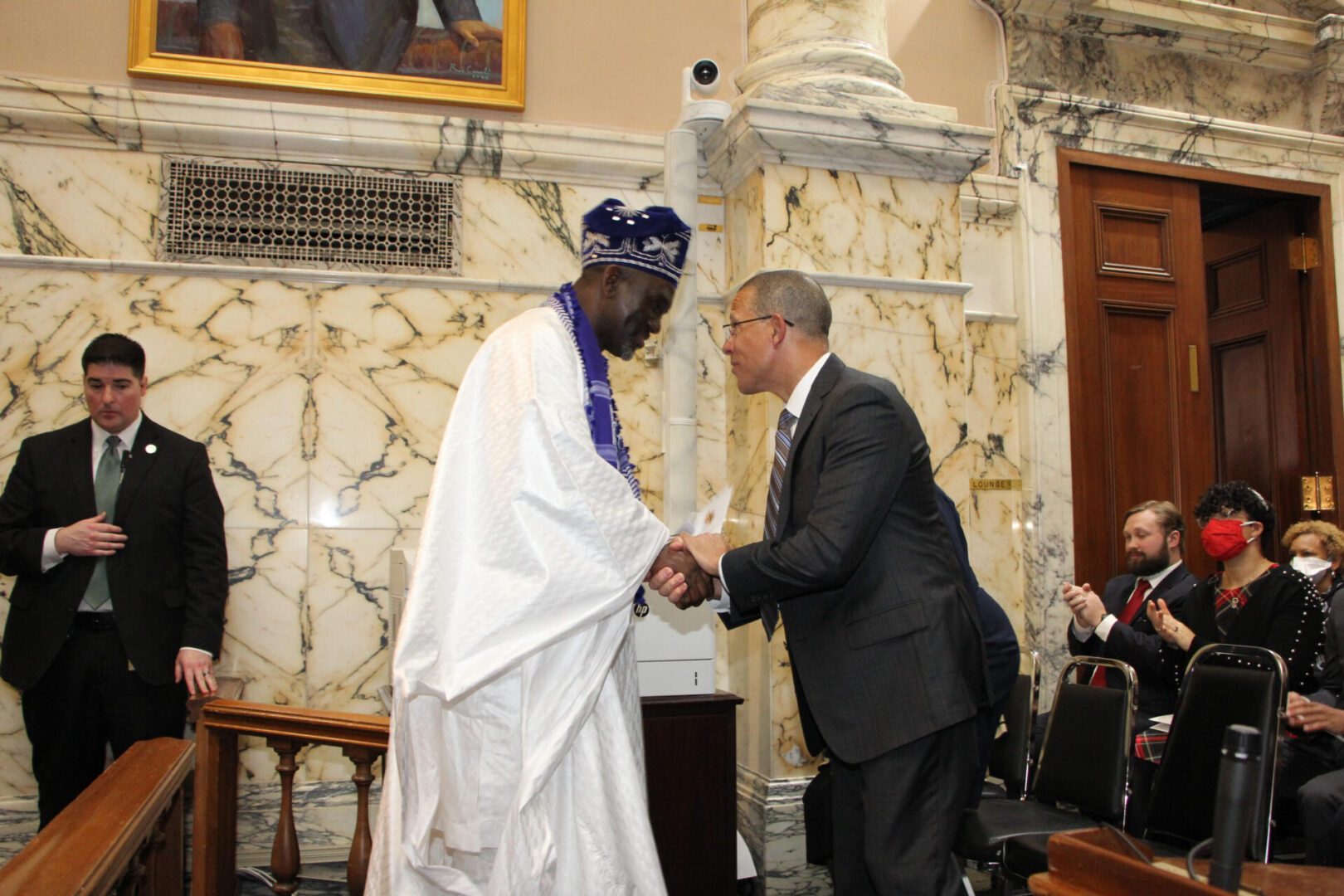 A man shaking hands with another man in front of a marble wall.