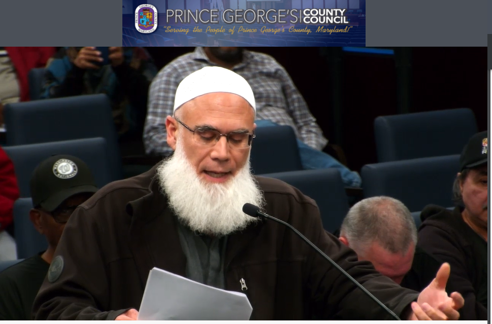 A man with a beard and a white beard speaking into a microphone.