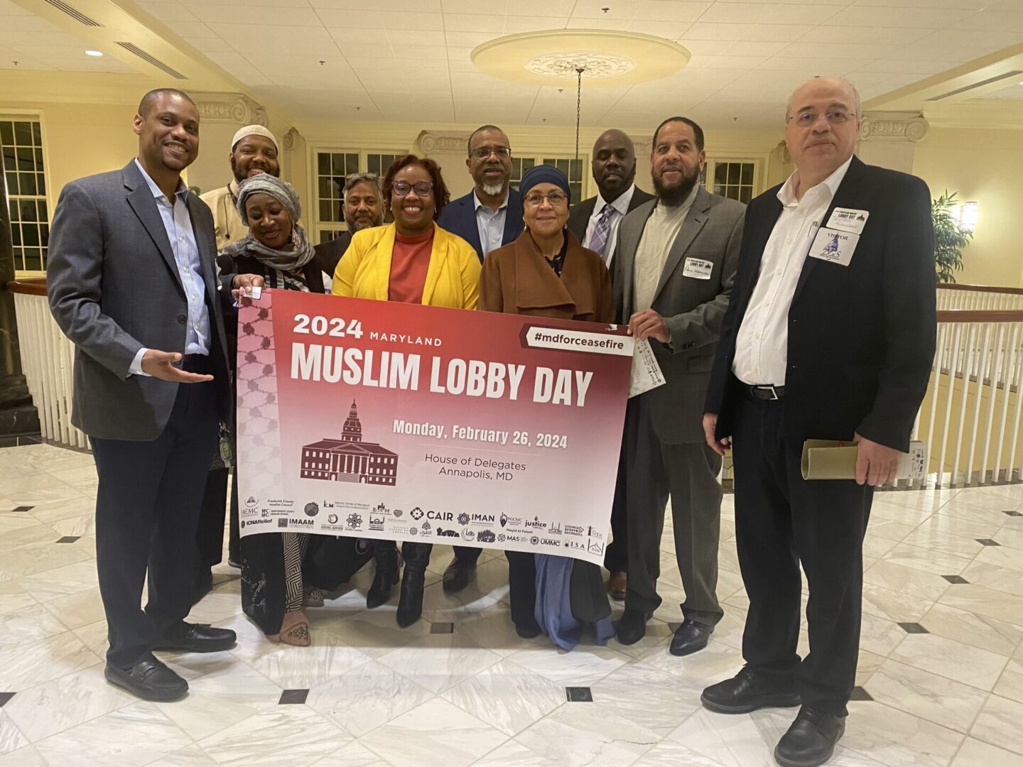 Group of individuals posing with a poster for maryland muslim lobby day 2024 in a lobby setting.