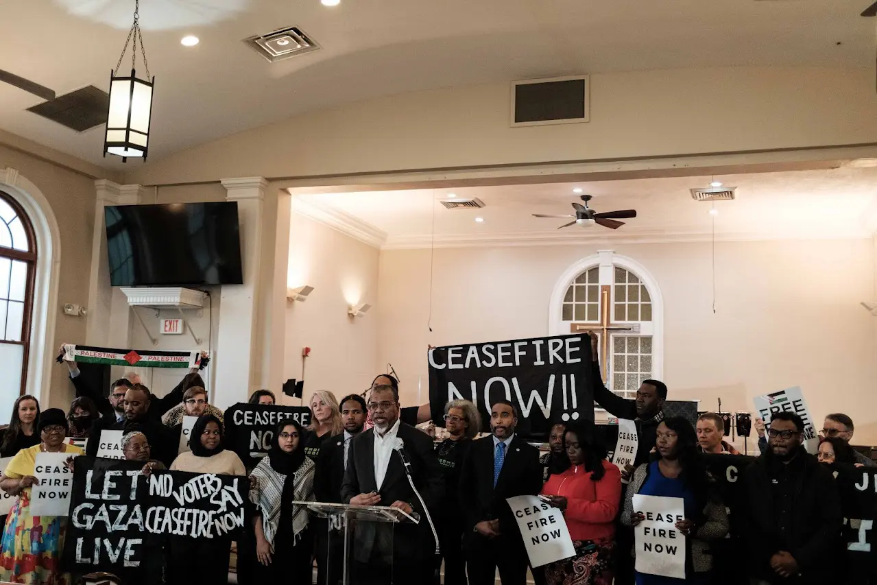 Group of individuals holding signs calling for a ceasefire, gathered in a room for a public event.